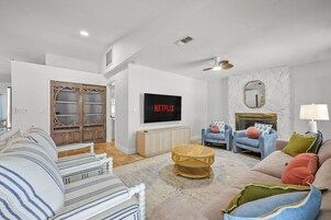 Un salón moderno con un televisor de pantalla plana, chimenea y diversas opciones de asientos, incluyendo un sofá, sillones y una mesa de centro de ratán.