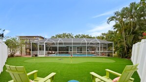A backyard with a pool, green lawn, and two green chairs. - 7-bedrooms Sports Court Pool Putt Putt (Seminole)