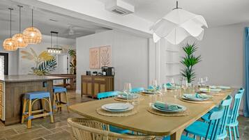Una cocina moderna con comedor, que incluye una mesa de madera dispuesta para seis personas, sillas azules y una zona de bar con taburetes de mimbre.