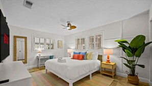 A hotel room with a bed, bedside tables, a desk, a chair, a ceiling fan, windows with shutters, a large plant, and a striped rug. - 7-bedrooms Sports Court Pool Putt Putt (Seminole)