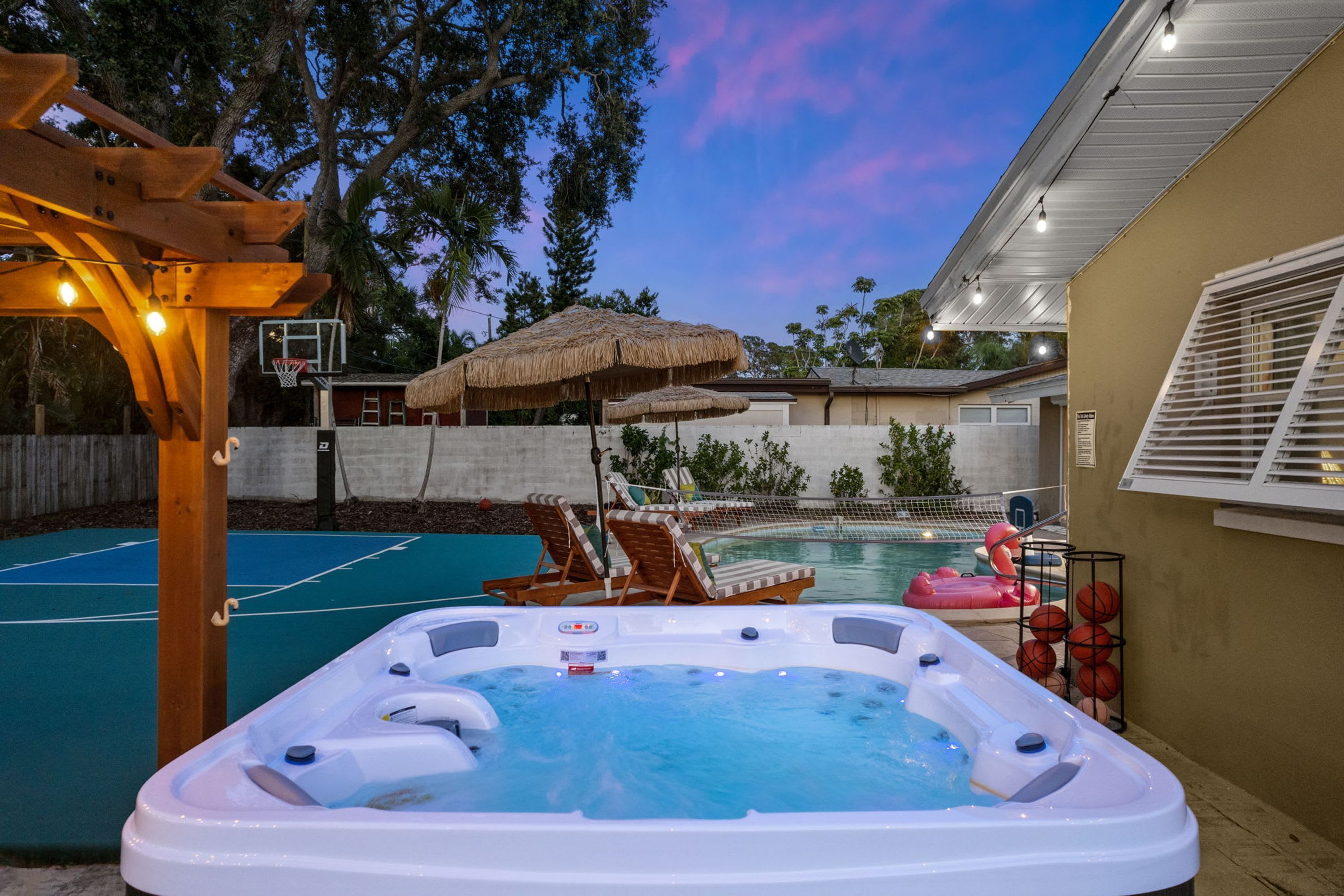 A backyard with a hot tub, a basketball court, and a pool.