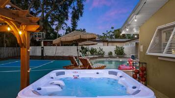 A backyard with a hot tub, a basketball court, and a pool.