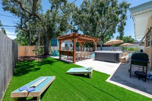 Ein Garten mit Kunstgrasanlage, einer Holz-Pergola, einem Whirlpool und einem Billardtisch.
