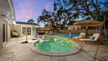 A backyard with a swimming pool, lounge chairs, and a hot tub.