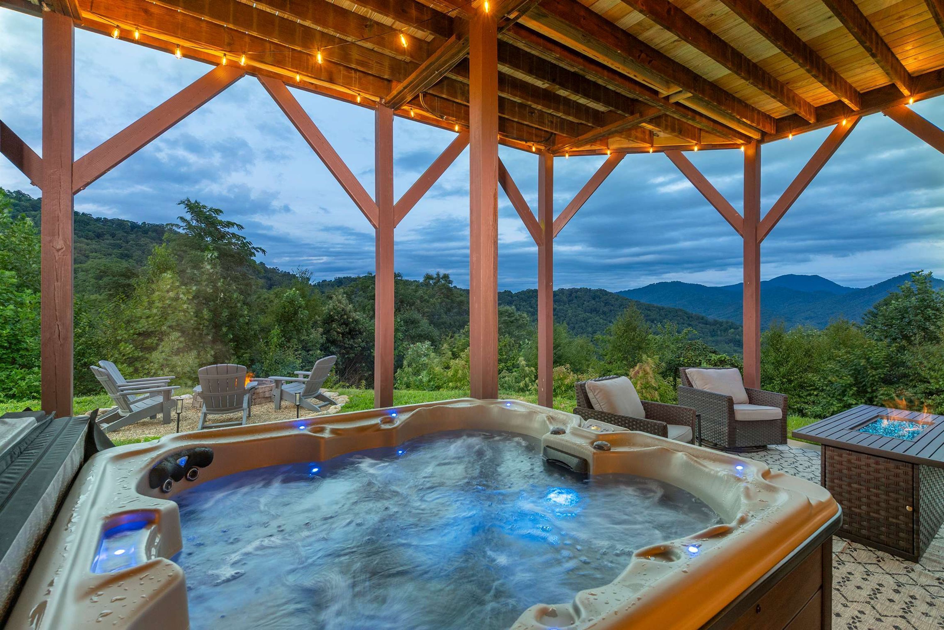 Ein Whirlpool mit Bergblick, umgeben von Holzliegen und einer überdachten Terrasse mit Lichterketten.