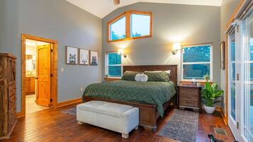 A bedroom with a wooden floor, a bed with a green quilt, a ceiling fan, and two windows with lamps.