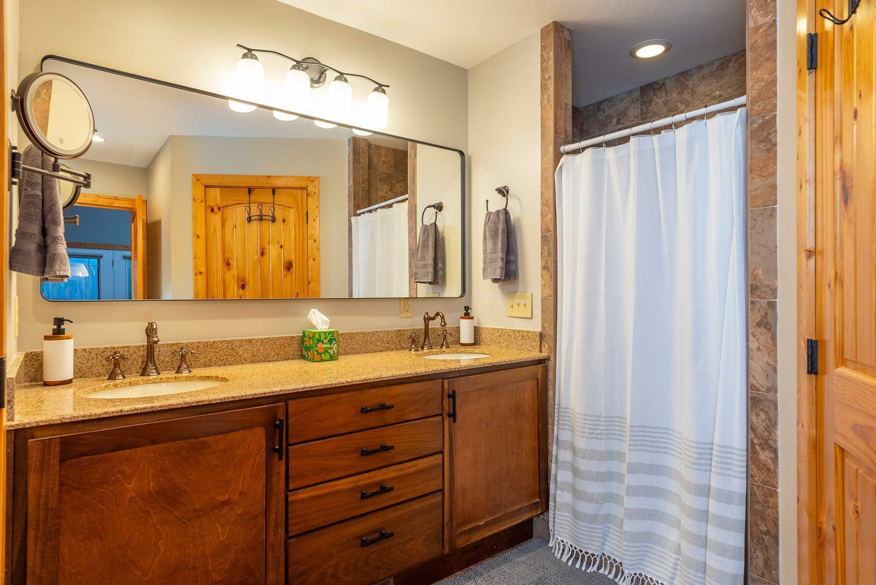 A bathroom with a wooden vanity, two sinks, a mirror, and a shower curtain.