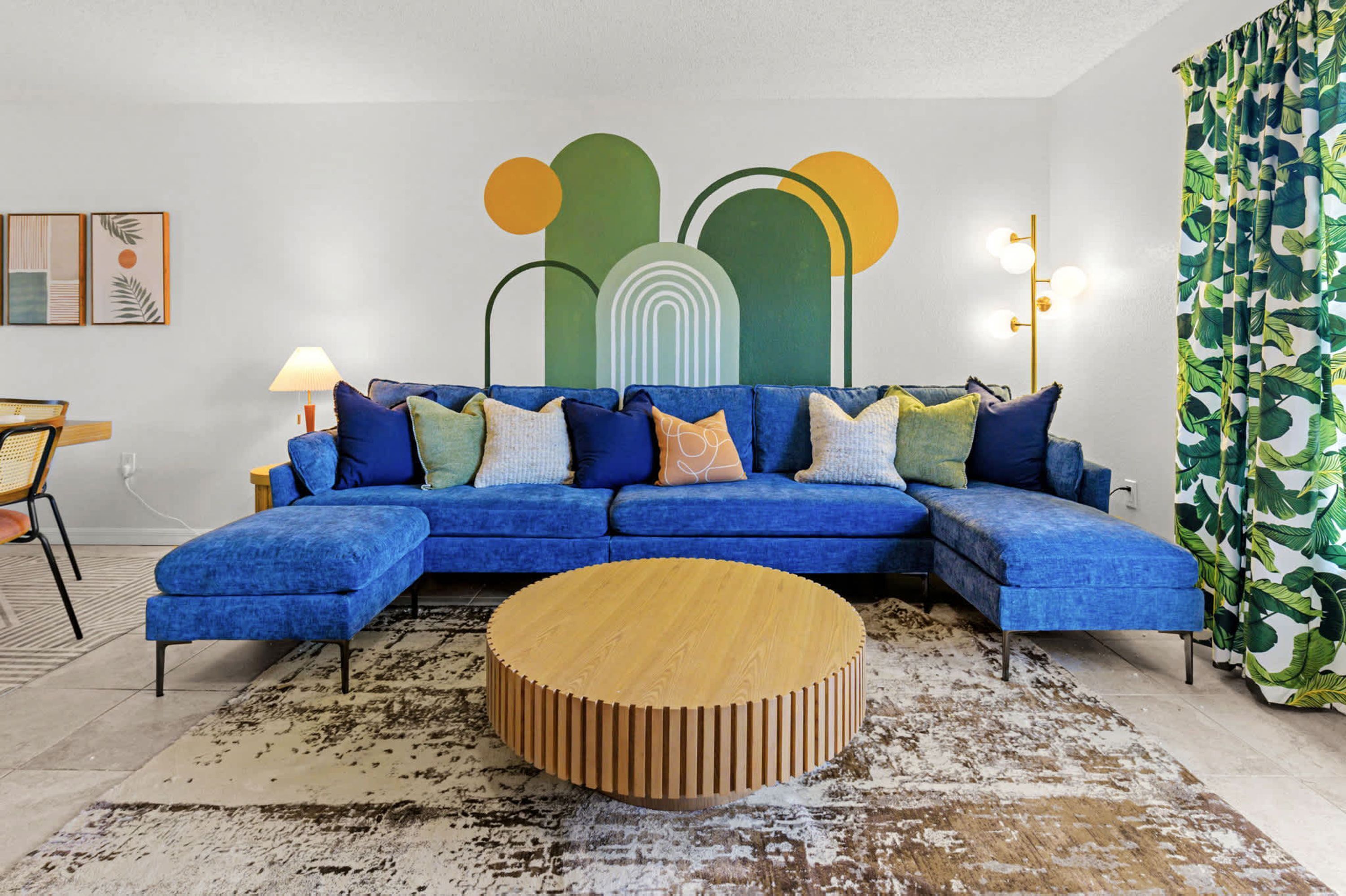 Un salon moderne avec un canapé d’angle bleu, une table basse en bois et des œuvres d’art abstraites accrochées au mur.