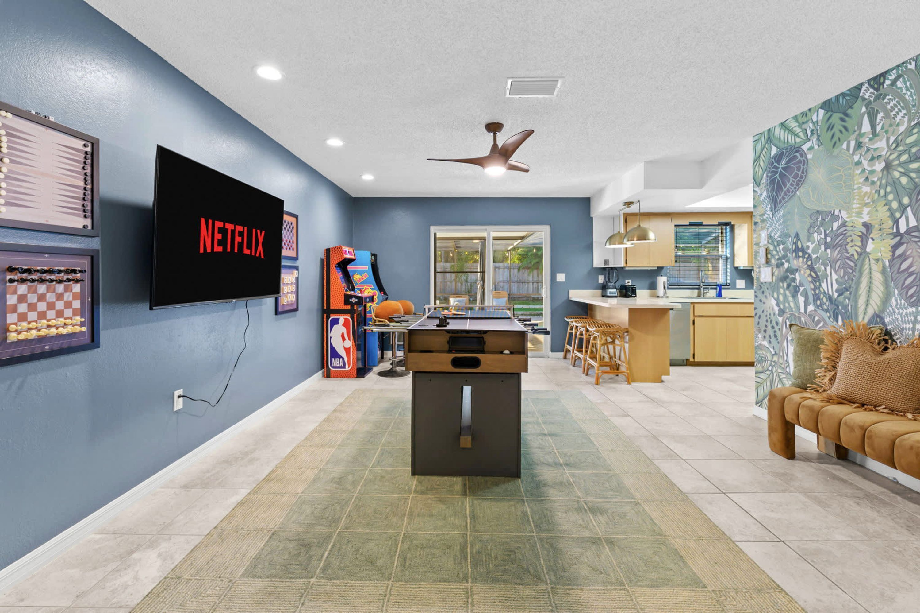 Una sala de estar con televisor de pantalla plana, mesa de futbolín y una zona de cocina con mesa de comedor y barra.