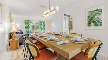 Comedor con una mesa de madera preparada para cuatro, rodeada de sillas de mimbre con cojines rojos.