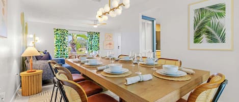 Un coin repas avec une table en bois dressée pour quatre personnes, entourée de chaises en osier avec des coussins rouges.
