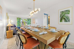 Comedor con una mesa de madera preparada para cuatro, rodeada de sillas de mimbre con cojines rojos.