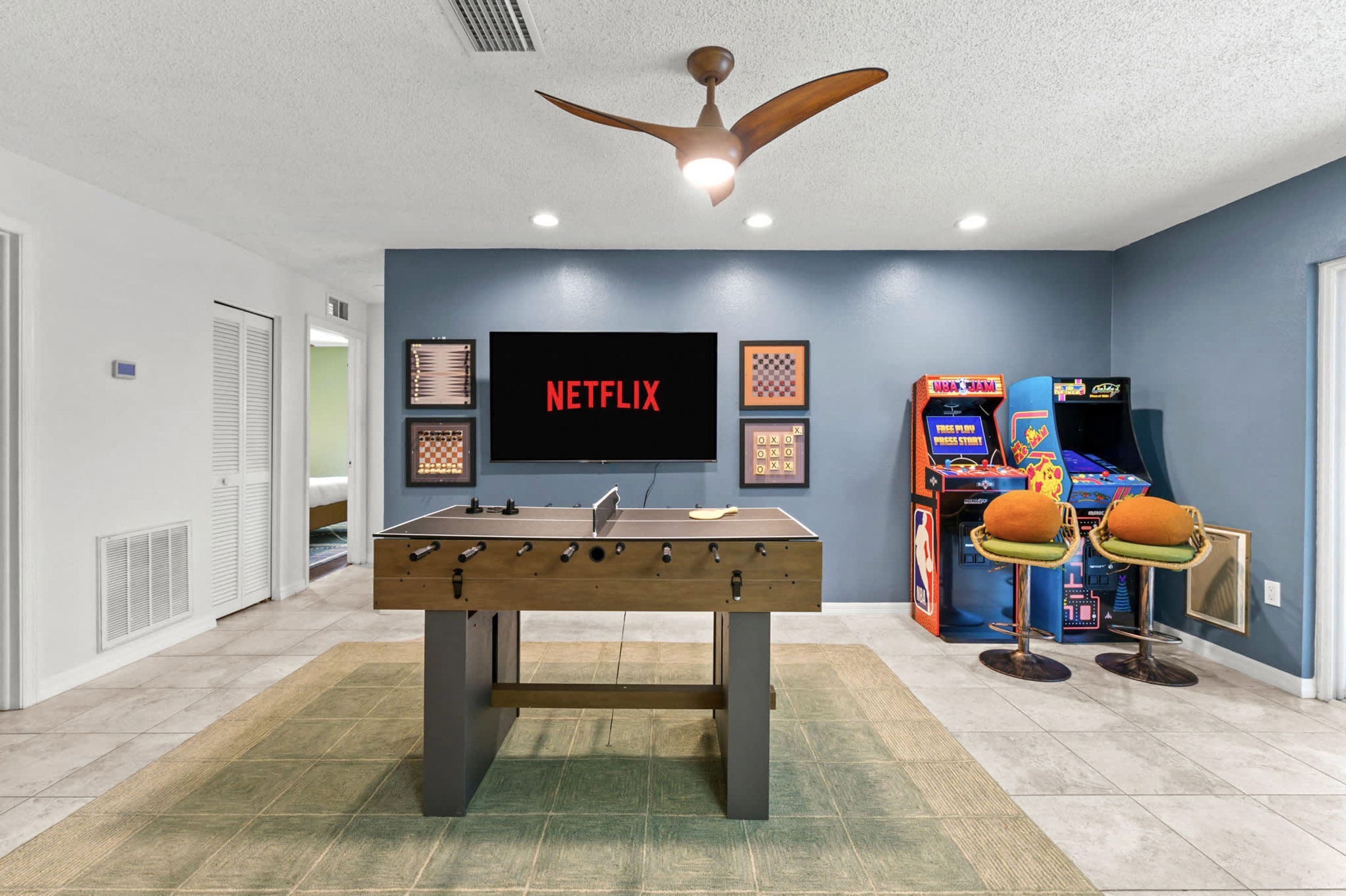 Una habitación con mesa de fútbol, televisor montado en la pared y juegos de arcade.