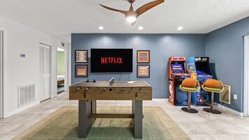 Una habitación con mesa de fútbol, televisor montado en la pared y juegos de arcade.