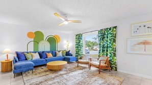 A living room with a blue sectional sofa, a round wooden coffee table, and a ceiling fan. - Pool Fire Pit Retreat Sleeps 14 - BBQ Grill (Largo)