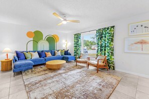 Ein Wohnzimmer mit einem blauen, modularen Sofa, einem runden Holztisch und einem Deckenventilator.