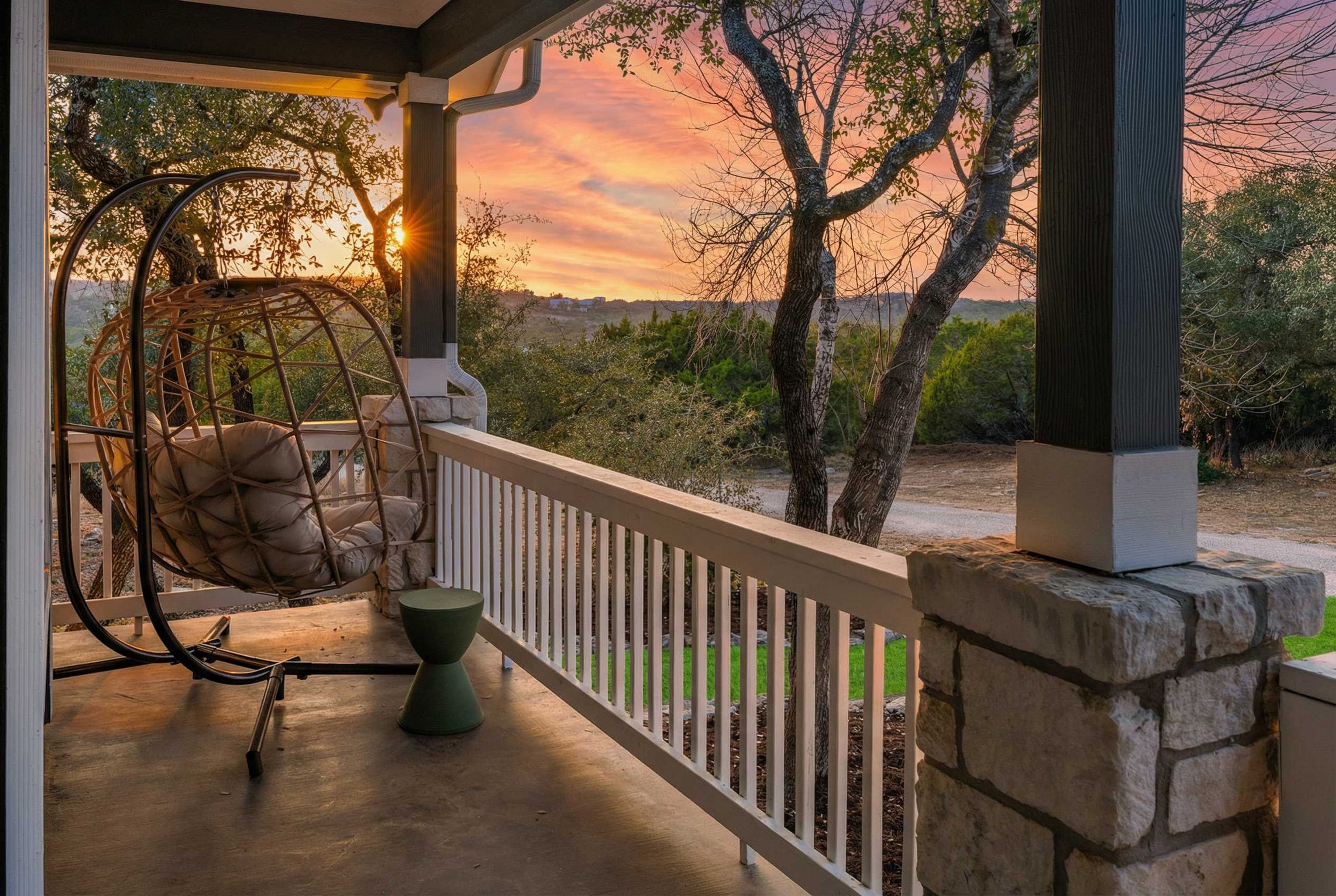 A porch with a swing chair, a table, and a view of the landscape.