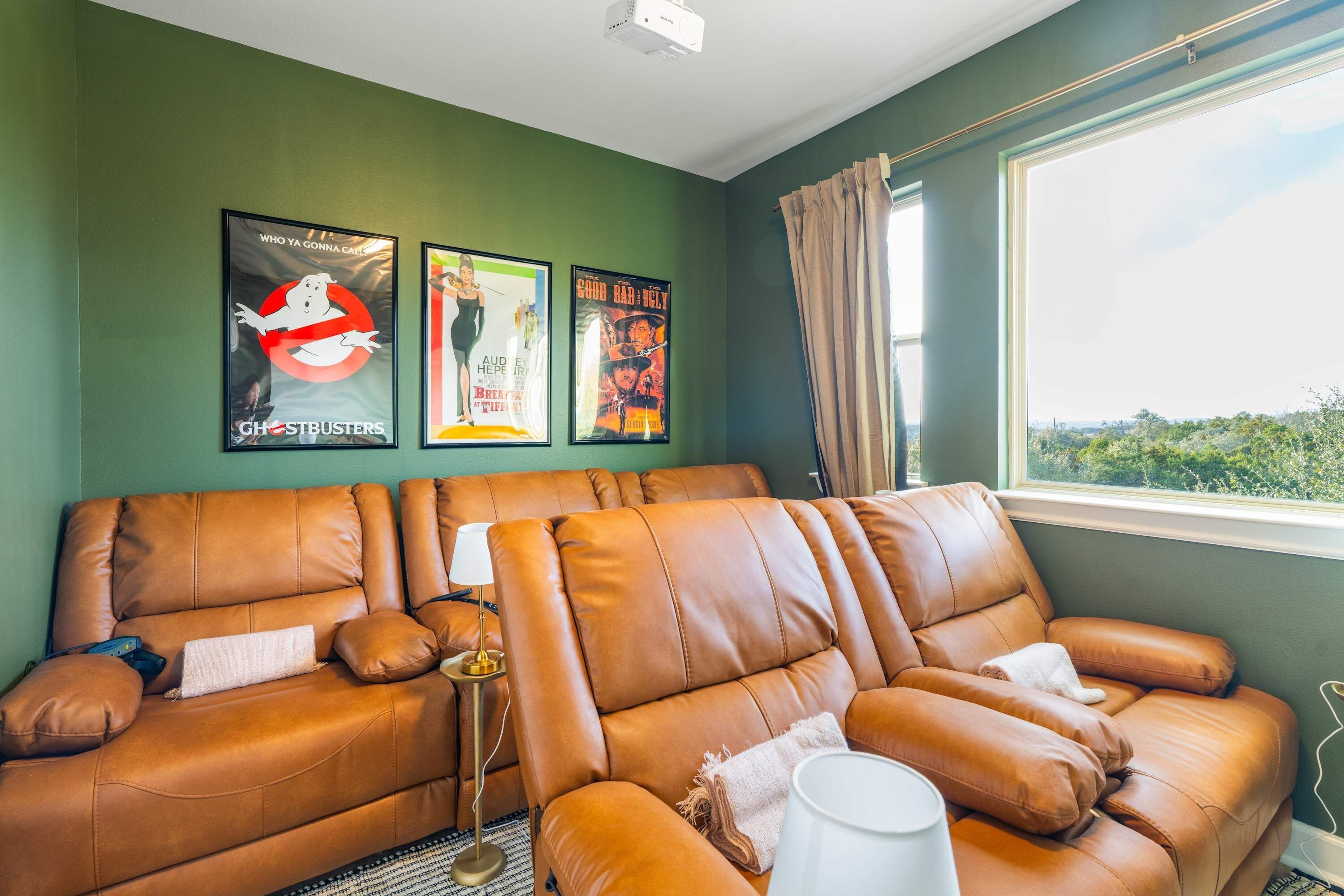 Une pièce avec un canapé en cuir marron, une lampe et trois affiches de films accrochées au mur.