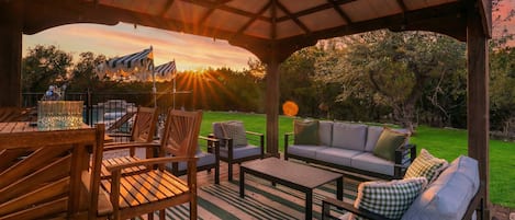 Un patio al aire libre con mobiliario de madera, una parrilla de barbacoa y vistas al atardecer.