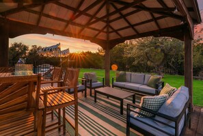 Eine Terrasse im Freien mit Holzmöbeln, einem Grill und Blick auf den Sonnenuntergang.