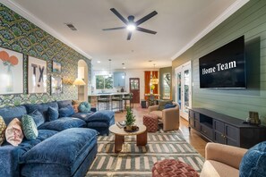 Ein modernes Wohnzimmer mit einer Couch, einem Couchtisch und einem Fernseher. Es gibt einen Essbereich mit Tisch und Stühlen.