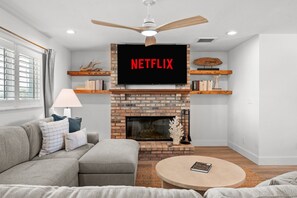 Een woonkamer met een open haard, een bank, een salontafel en een tv boven de open haard, waarop 'NETFLIX' wordt weergegeven.