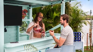 A person pouring a drink from a pitcher into a glass, another person holding a drink, and a table with chairs in a light blue outdoor setting. - Waterfront Walk to Beach Pool Kayaks Bikes (Indian Rocks Beach)