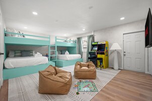Una habitación con literas, una consola de videojuegos, pufs y un juego de mesa Monopoly.