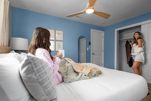 Ein Schlafzimmer mit einem Bett, einem Deckenventilator, einer Tür und einer Wand mit gerahmten Bildern.