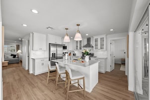 Una cocina moderna con armarios blancos, una isla central con taburetes de bar, electrodomésticos de acero inoxidable e iluminación colgante.