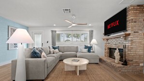 A modern living room with a sectional sofa, a fireplace, a flat-screen TV, and a ceiling fan. - Waterfront Walk to Beach Pool Kayaks Bikes (Indian Rocks Beach)
