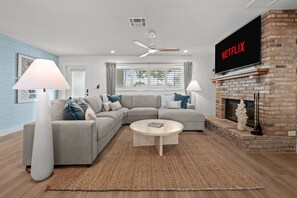 Ein modernes Wohnzimmer mit Ecksofa, Kamin, Flachbildfernseher und Deckenventilator.