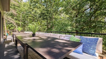 Una terraza con una mesa larga y un sofá, rodeada de abundante vegetación.