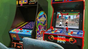 Dos máquinas de arcade, una de Pac-Man y otra de Mortal Kombat, frente a un muro verde.