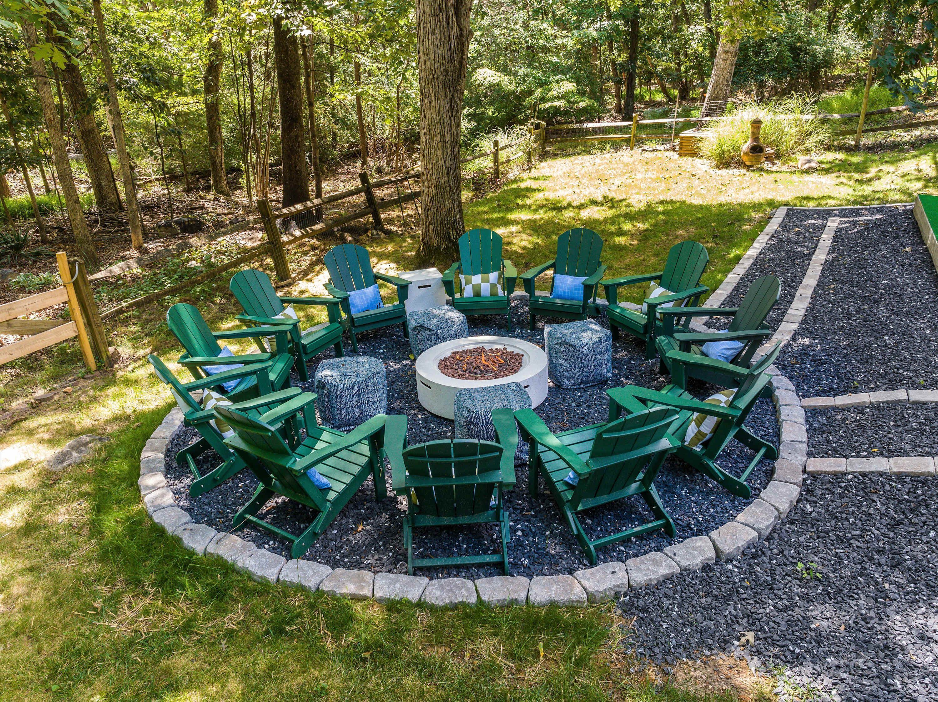 A circular outdoor seating area with Adirondack chairs and a central fire pit surrounded by a gravel border.