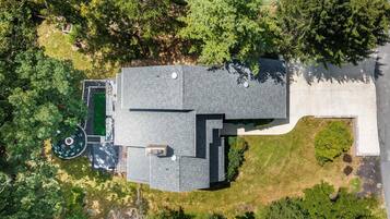 An aerial view of a residential property with a large house, a swimming pool, and surrounding greenery.
