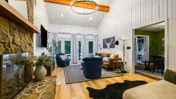 A spacious living room with a stone fireplace, a chandelier, and a view of the outdoors through large windows.