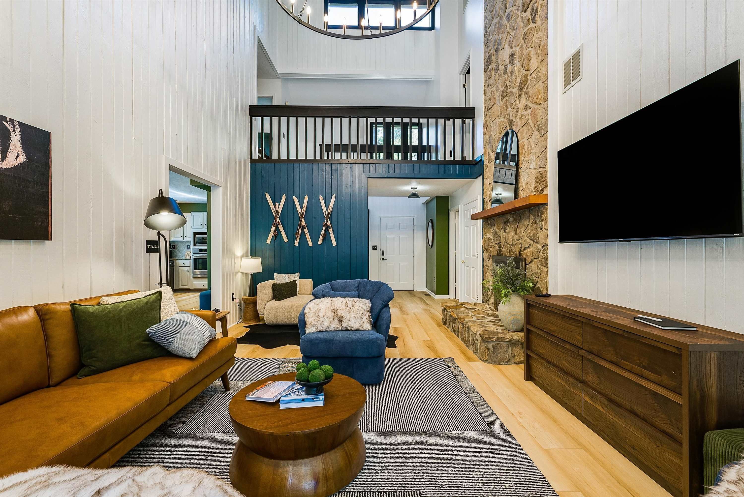 Un salón amplio con techo alto, un televisor grande y una escalera que conduce a un nivel superior.