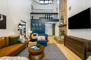A spacious living room with a high ceiling, a large TV, and a staircase leading to an upper level. - Modern Peaks Hot Tub Sauna Theatre Room (McGaheysville)