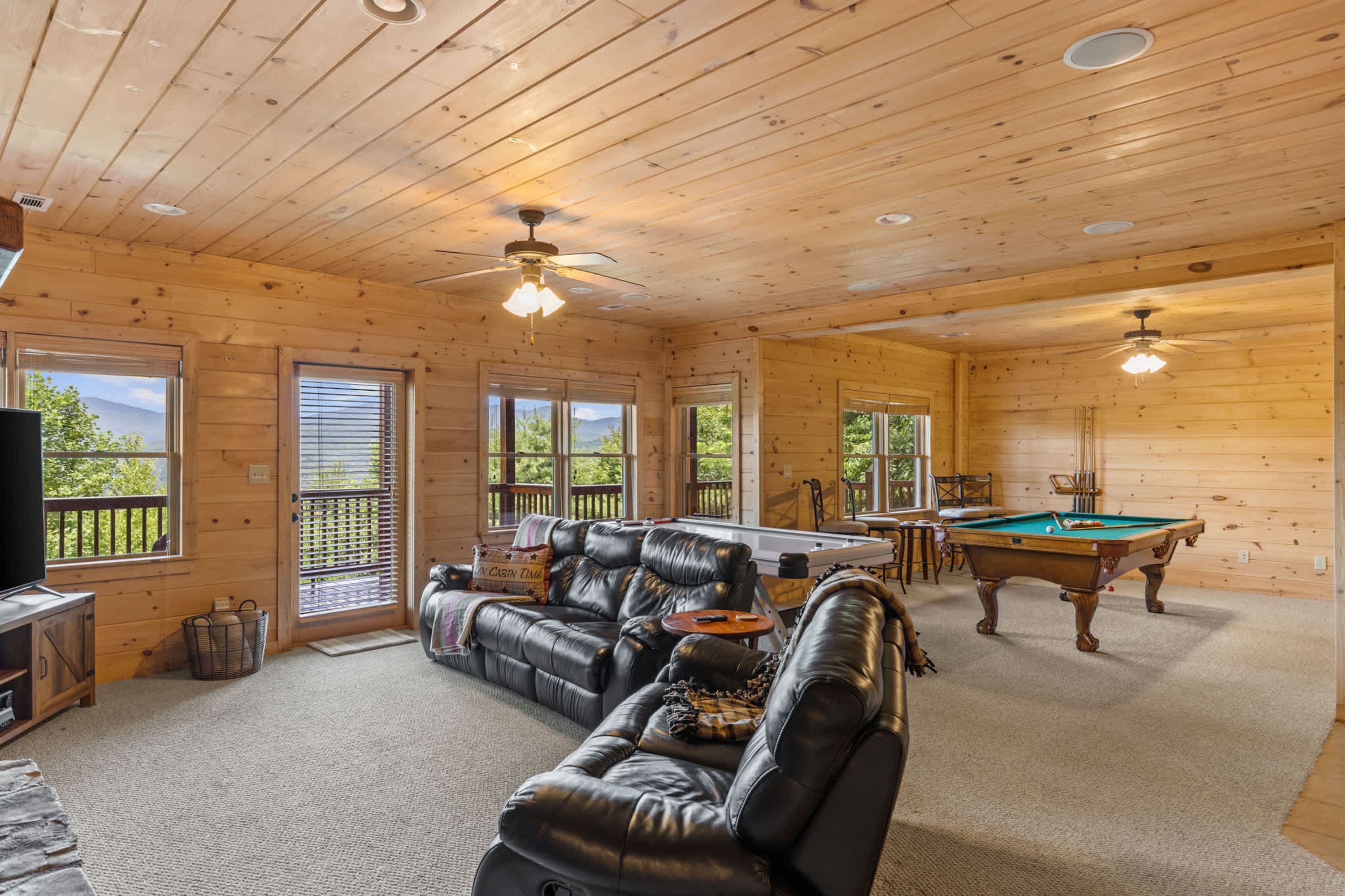 Interior de una cabaña de madera con mesa de billar, sofá de cuero y televisor.
