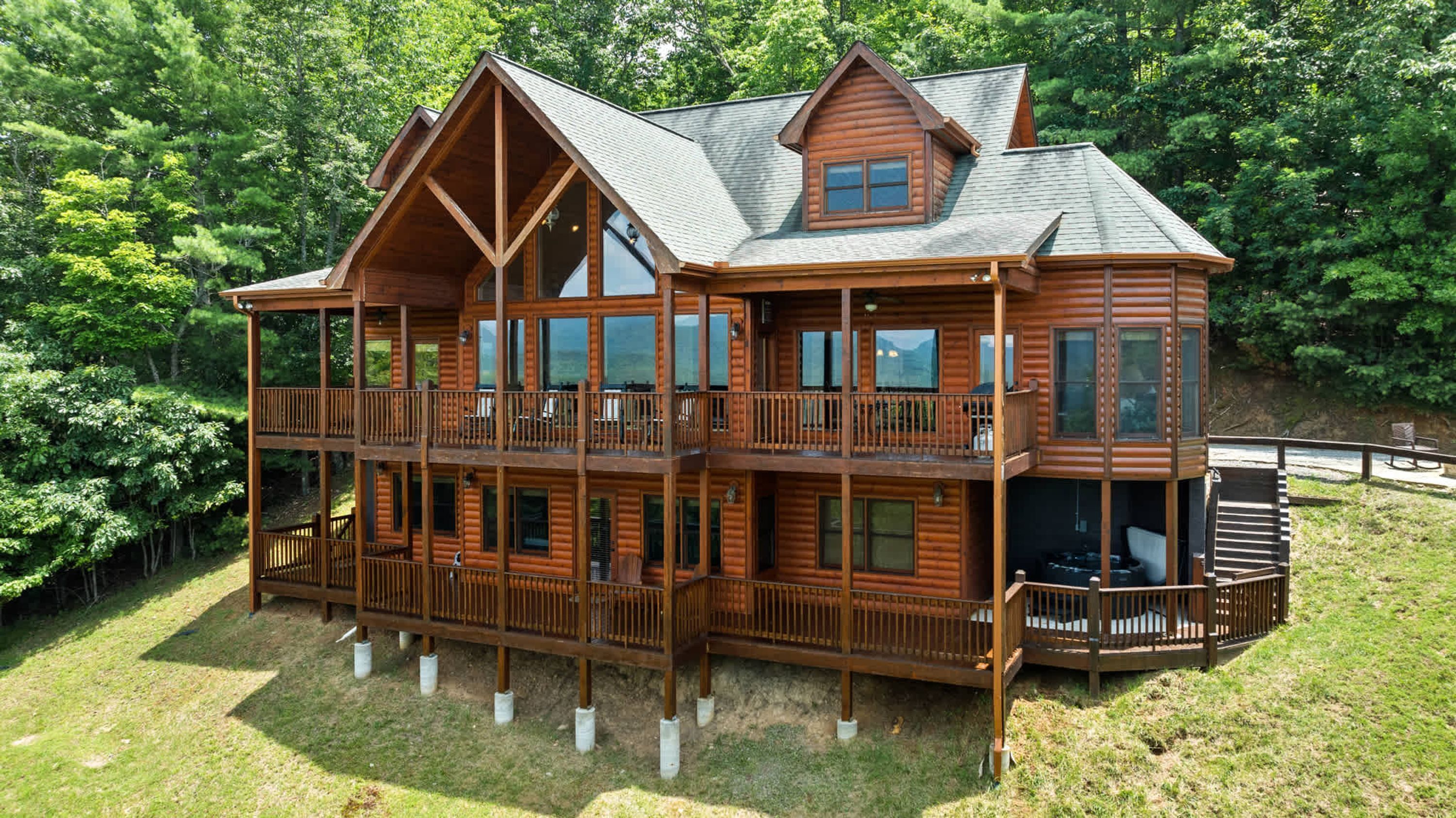 Une grande cabane en rondins à plusieurs étages, dotée d’un balcon au deuxième étage et entourée d’une zone boisée.