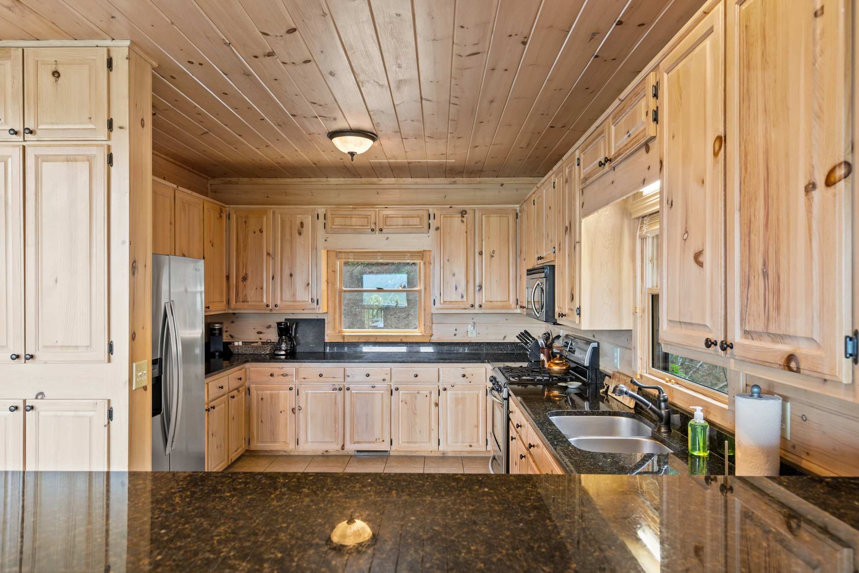A kitchen with wooden cabinets, a stainless steel refrigerator, a stove, and a window.