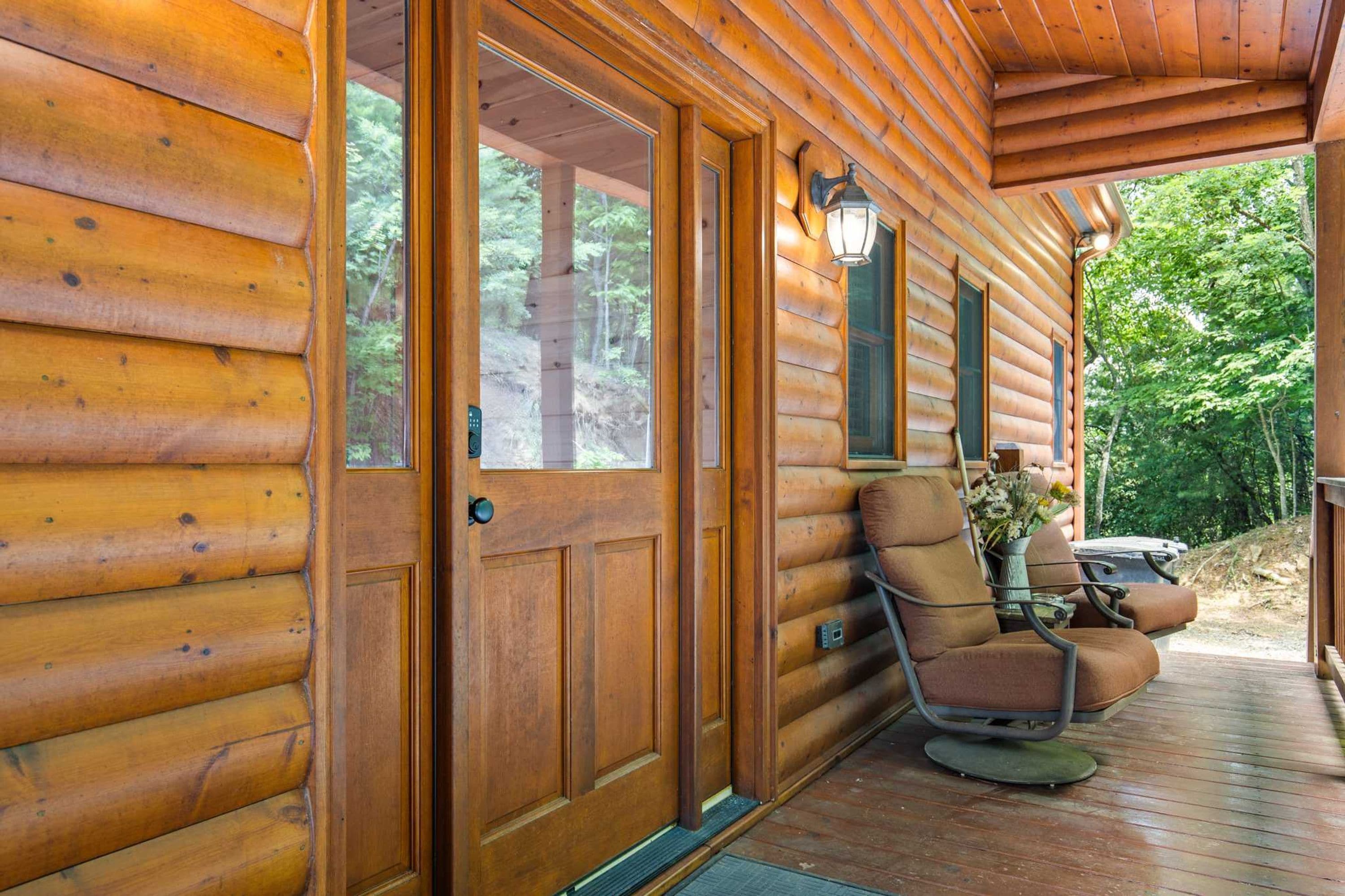 Une cabane en bois avec une véranda, un fauteuil à bascule et une table ornée d’un vase de fleurs.