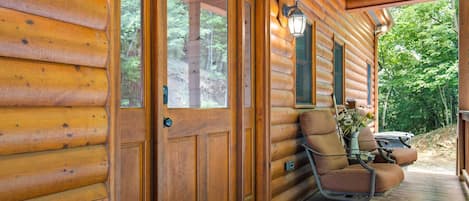 Une cabane en bois avec une véranda, un fauteuil à bascule et une table ornée d’un vase de fleurs.
