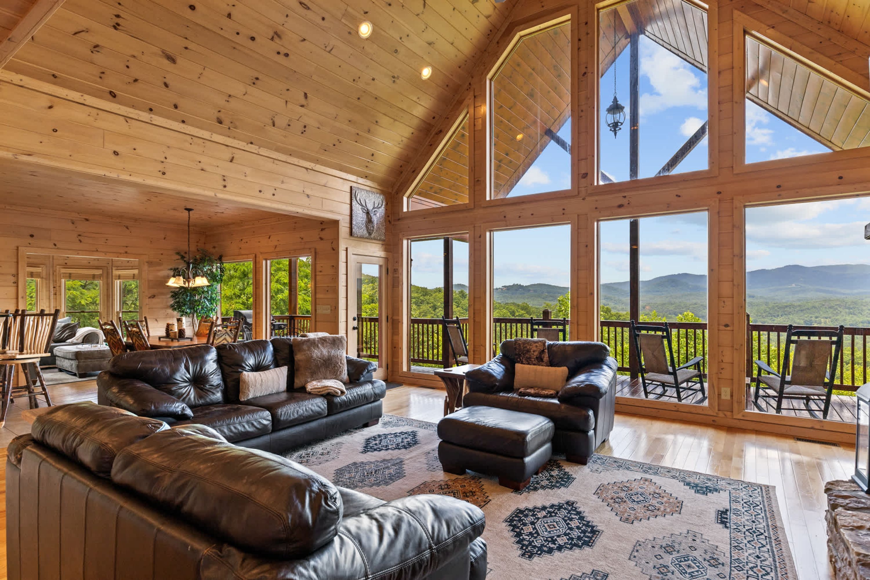 Ein geräumiges Wohnzimmer mit Ledersofas, einem großen Teppich und Blick auf eine gebirgige Landschaft durch große Fenster.
