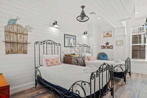 A bedroom with two beds, a wooden wall, a ceiling fan, and a window with blinds. - Island Star Private Pool 5BR Beach Access (Port Aransas)