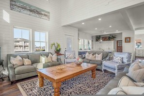 A spacious living room with a large wooden coffee table, multiple seating options including sofas and chairs, and a patterned rug. - Island Star Private Pool 5BR Beach Access (Port Aransas)