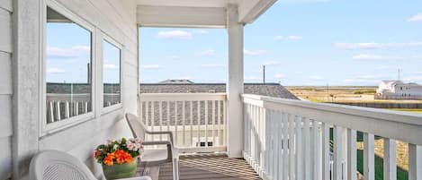 A covered porch with a view of the beach and a distant building.