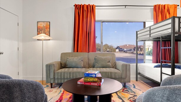 Ett rum med en soffa, ett soffbord med brädspel, en våningssäng och ett fönster med gardiner.