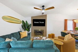 A living room with a sofa, coffee table, and a television labeled 'Home Team.' - Poolside Oasis Sleeps 8 Game Room Putt Putt (Bradenton)